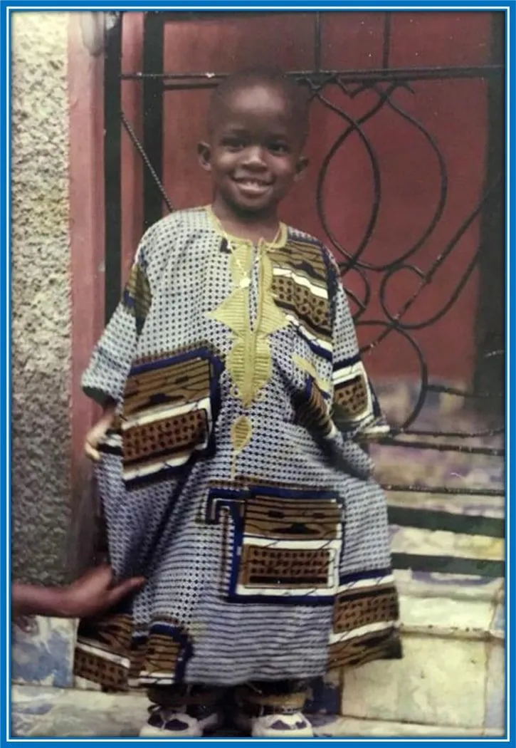 On this day, not many knew he would be a Premier League footballer. A smiling Doucour&eacute; takes a photo in front of his family home.