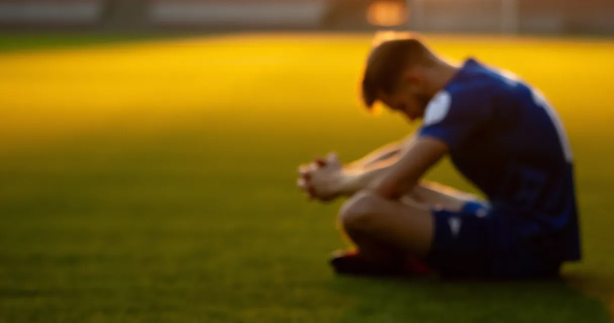 Footballer sitting alone on pitch at sunset in emotional moment
