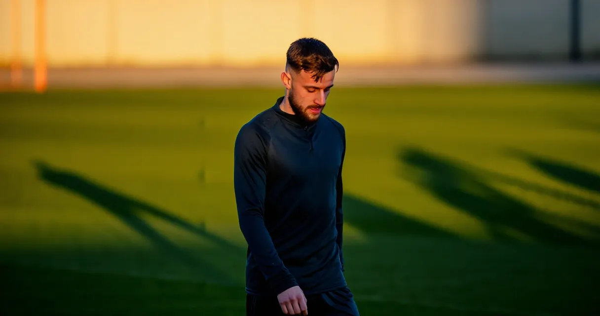 Footballer standing alone on pitch at sunset, marking the end of a career