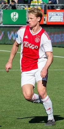 Voetballer traint op een zonnig voetbalveld, stadion op de achtergrond