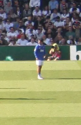 Premier League forward in blue kit dribbling at speed in a packed floodlit stadium
