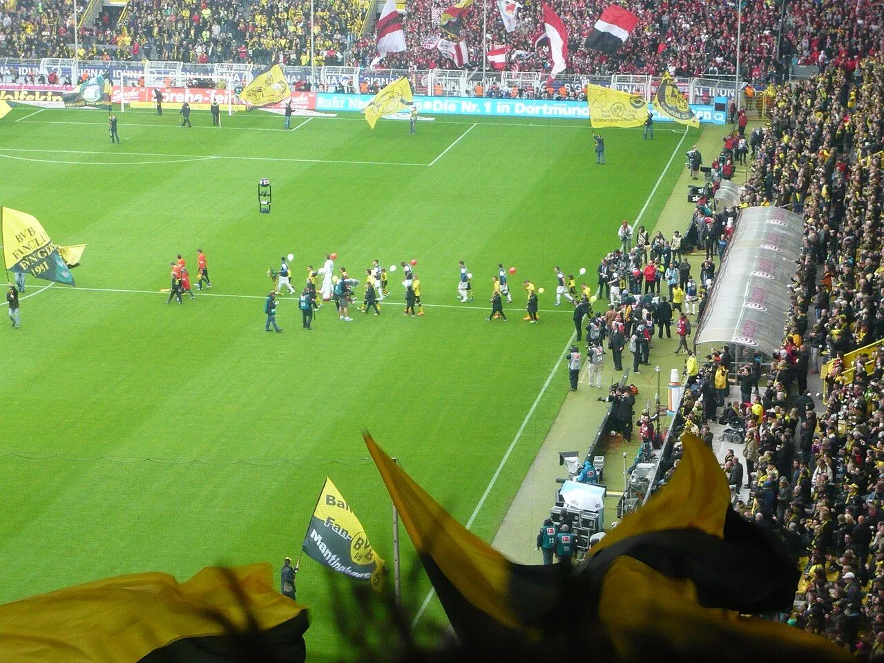Football players compete for the ball in a packed, floodlit stadium at night