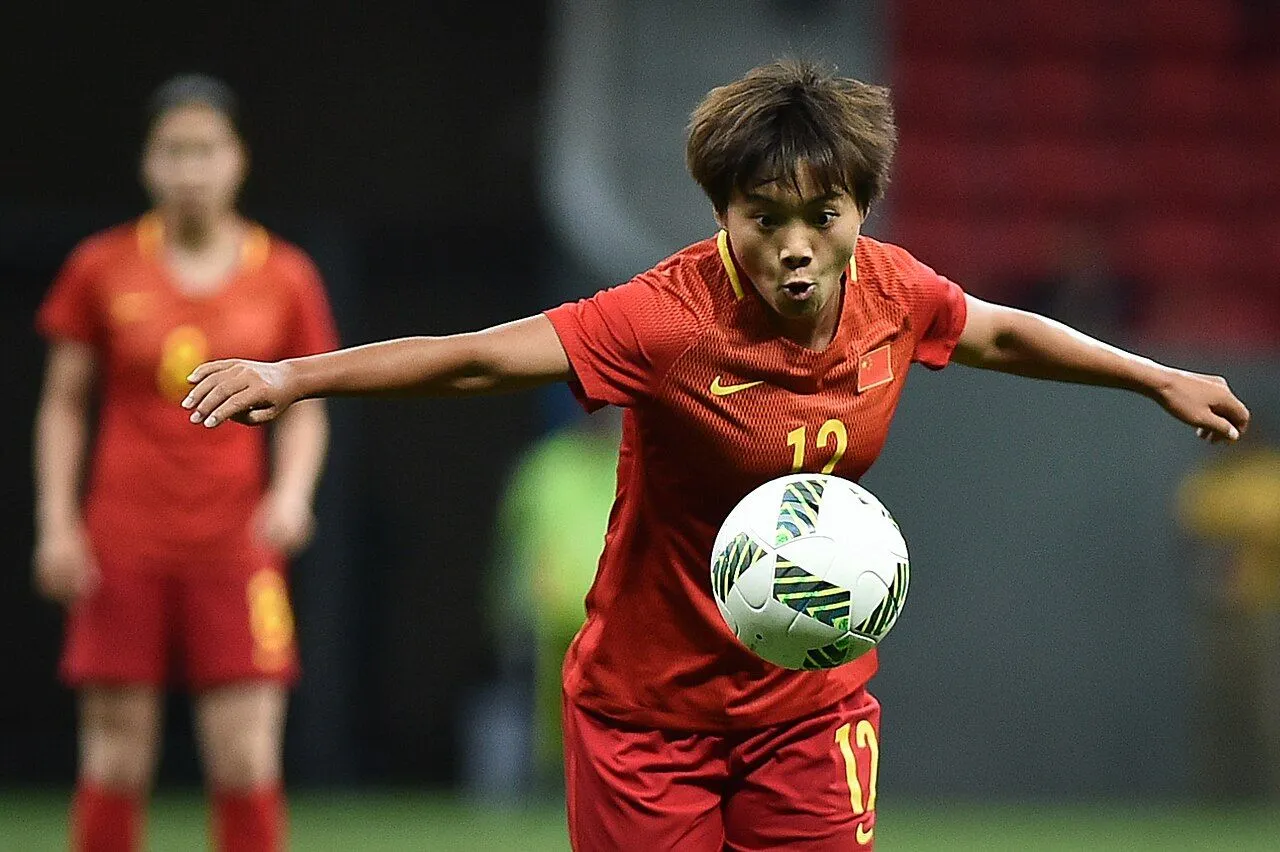 Female footballer scoring a goal under floodlights in a packed stadium